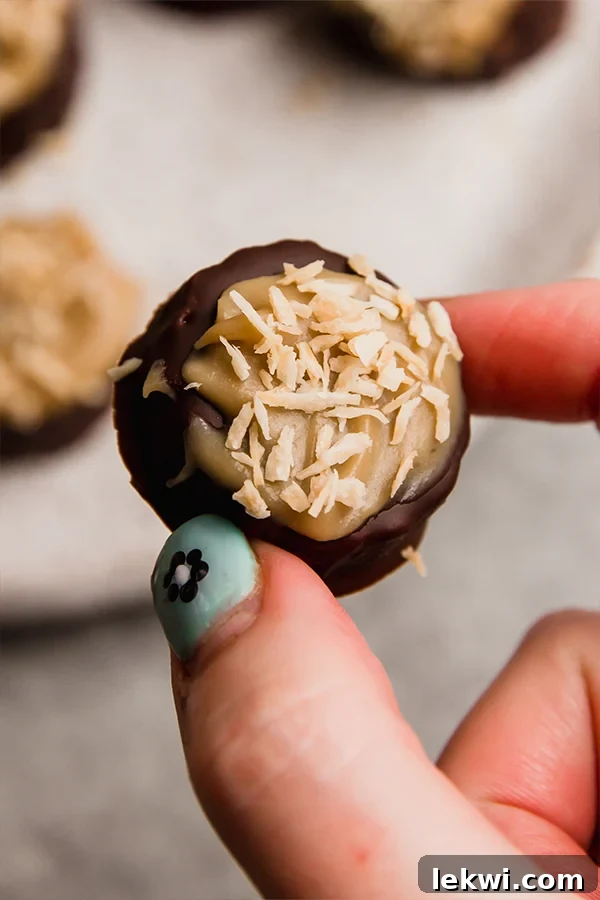 A hand gently holding a single Samoa Banana Bite, showing the perfect layers of chocolate, caramel, and toasted coconut.