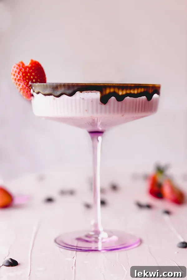 Tall-stemmed glass featuring a creamy pink chocolate-covered strawberry mocktail, with a generous chocolate rim and a fresh strawberry garnish.