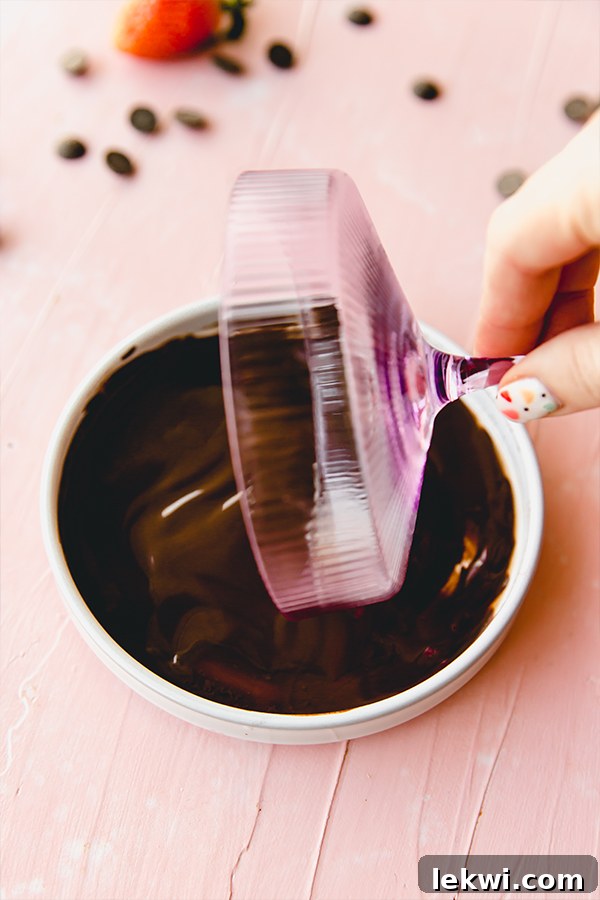 A hand expertly twirling a pink cocktail cup in melted chocolate to create a perfect rim.