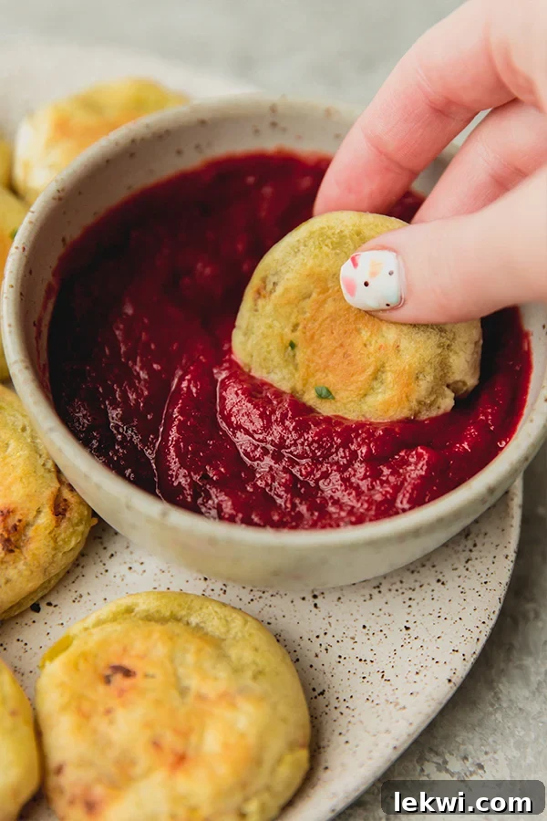 A hand dipping a golden-brown AIP pizza roll into a small white bowl of red nightshade-free marinara sauce.