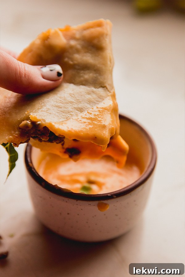 A hand dipping a crispy baked ground beef taco into a bowl of creamy dairy-free cheese sauce.