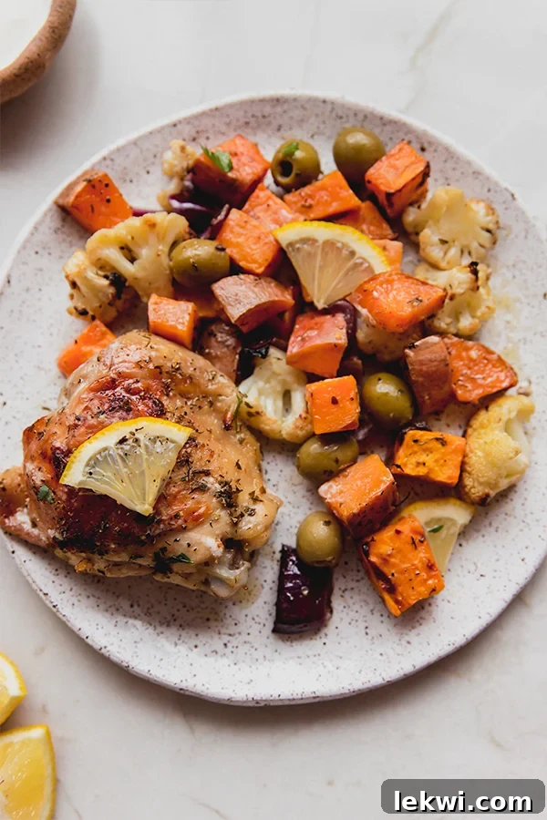 A single serving plate featuring golden-brown Mediterranean chicken, roasted sweet potatoes, cauliflower, and red onion, garnished with fresh herbs.
