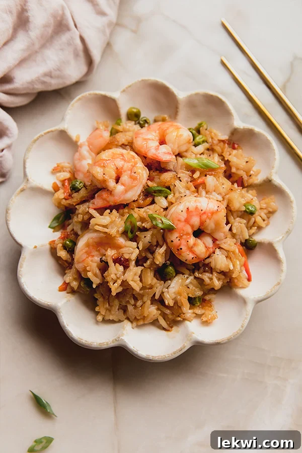 A beautifully plated serving of sheet pan shrimp fried rice, garnished with fresh herbs, resting on a rustic wooden counter.