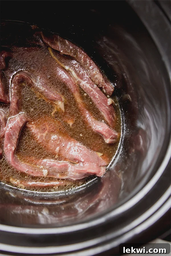 Strips of beef in a slow cooker, seasoned and ready for cooking.