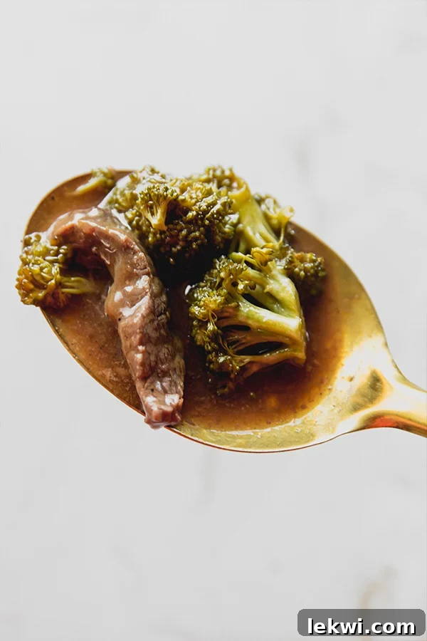 Spoon with a scoop of orange beef and broccoli, showing the rich sauce and tender ingredients.