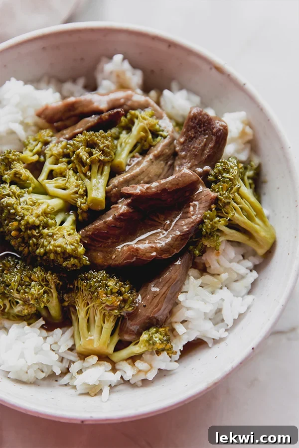 Bowl of rice topped with orange beef and broccoli, garnished and ready to eat.
