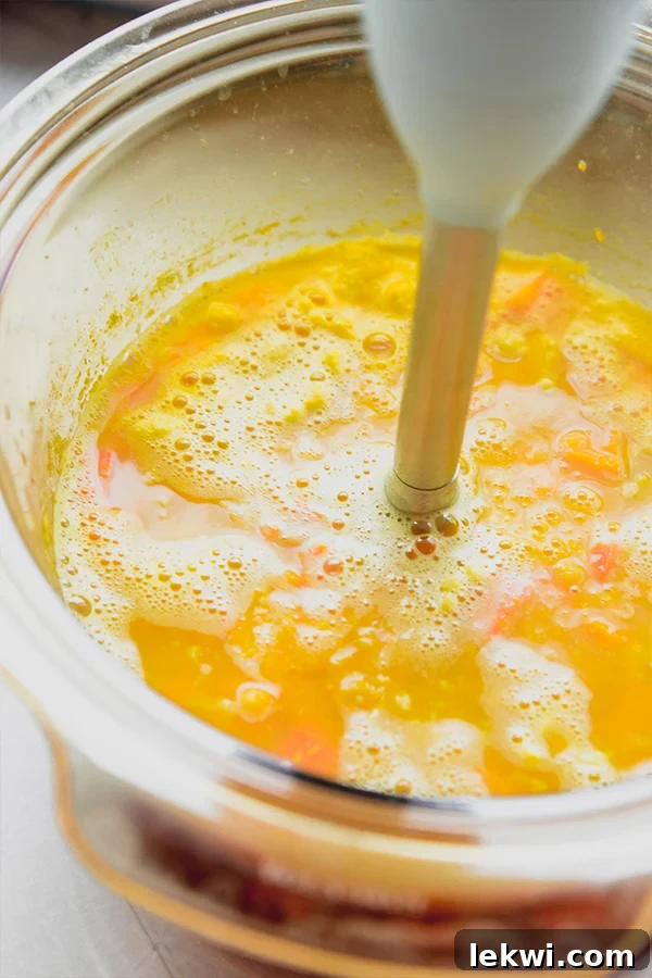 An immersion blender being used to puree the golden chickpea and veggie soup in the slow cooker.