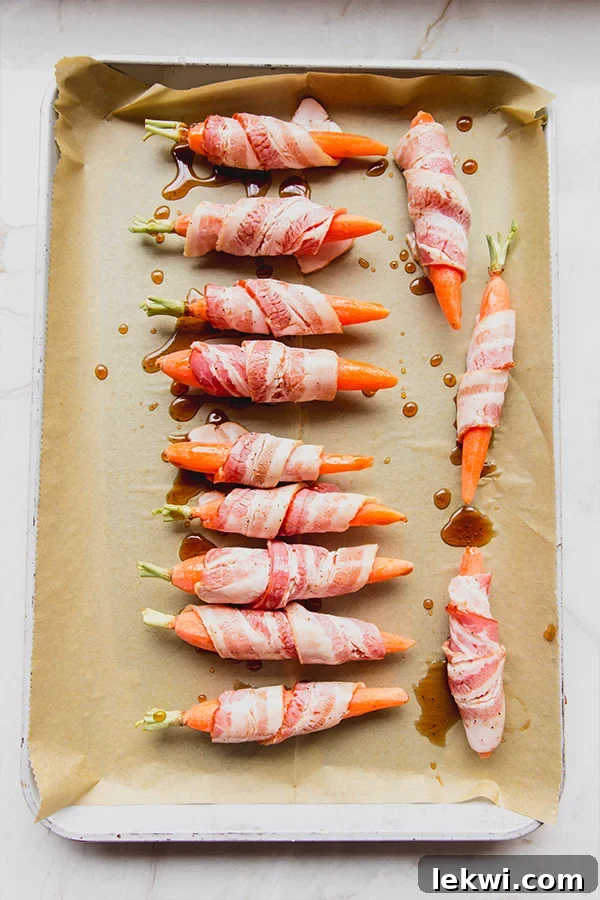 Several bacon-wrapped carrots arranged neatly on a parchment-lined baking sheet, ready for the oven.