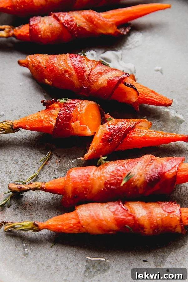 A close-up of several bacon-wrapped carrots on a white plate, with one cut in half to show the tender carrot inside.