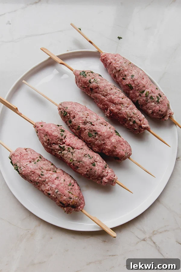 Several raw beef kofta skewers arranged on a plate.