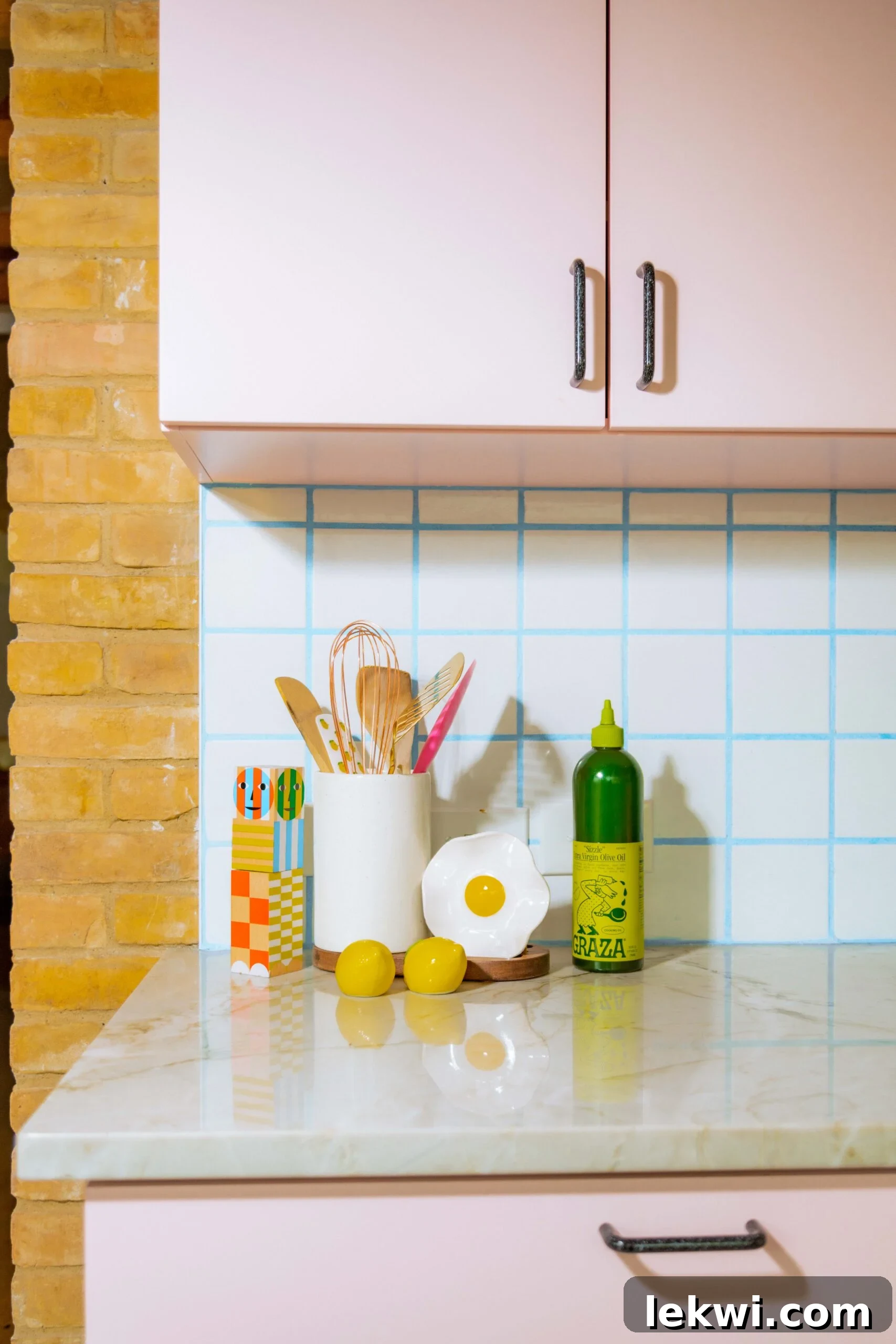 After renovation: Cooking utensils neatly arranged on a light quartzite countertop in the stylish pink kitchen, emphasizing functionality.