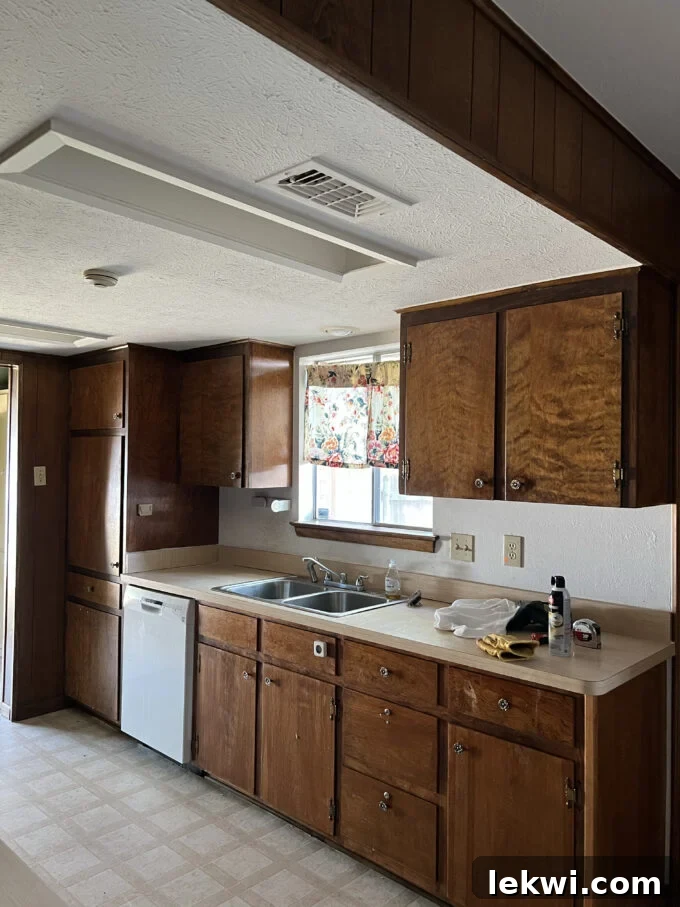 Before renovation: Kitchen with dark brown cabinets, a drop ceiling, and an old-fashioned aesthetic.