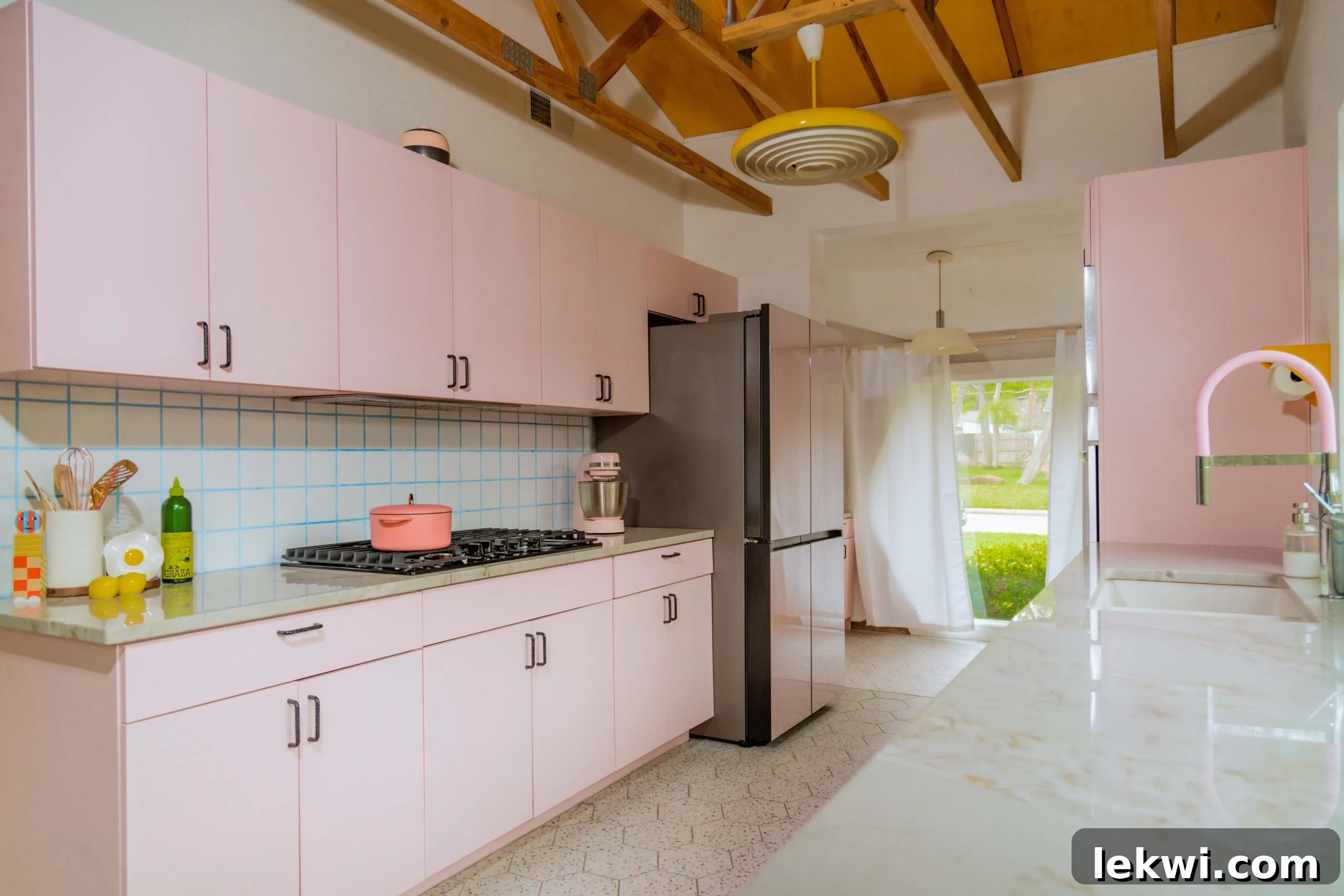 After renovation: A bright kitchen featuring pink cabinets, light countertops, and stylish mid-century modern design elements.