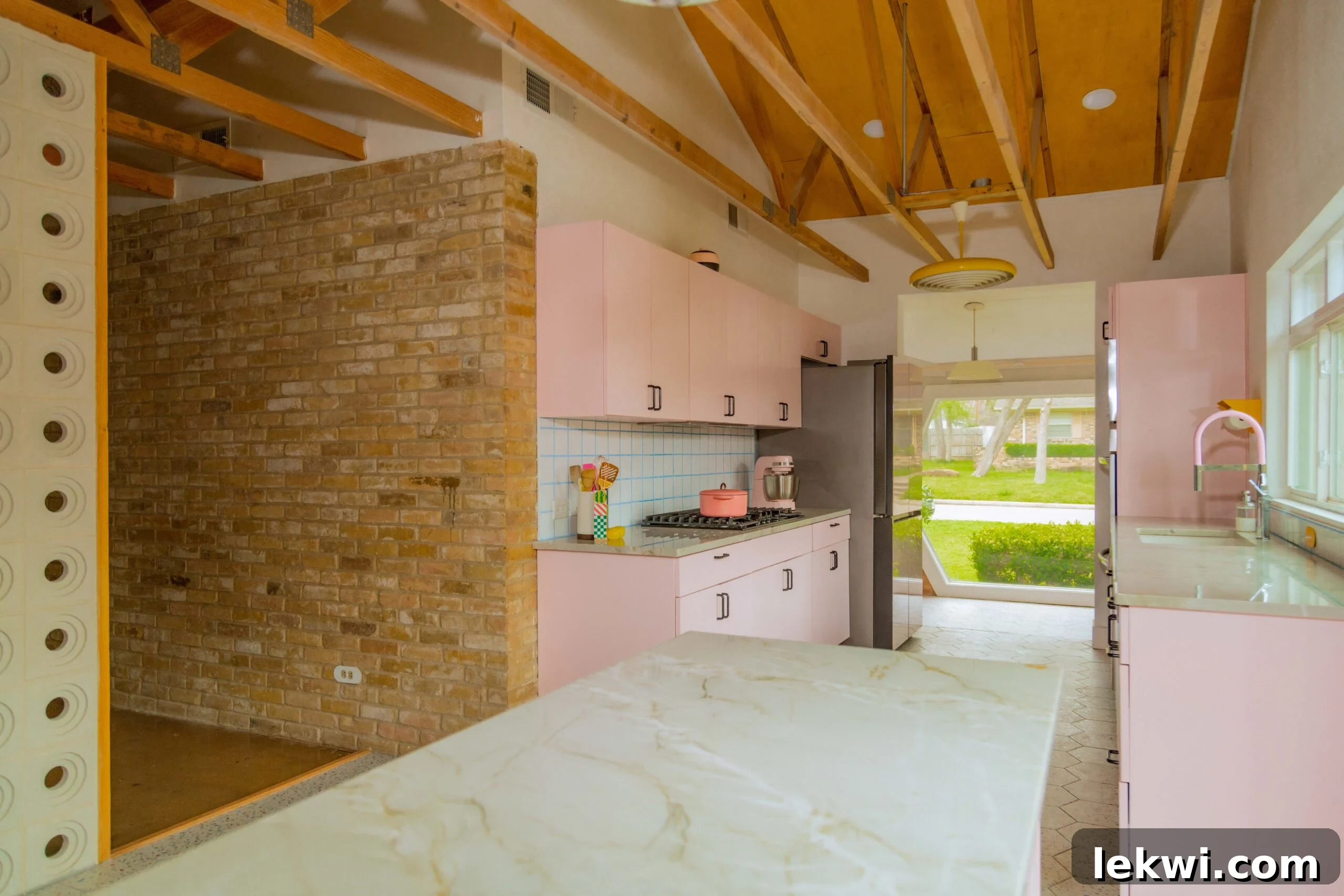 After renovation: Pink kitchen cabinets adjacent to an exposed brick wall, adding texture and character to the mid-century modern design.