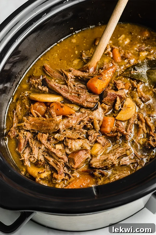 Wooden spoon in a slow cooker of pot roast.