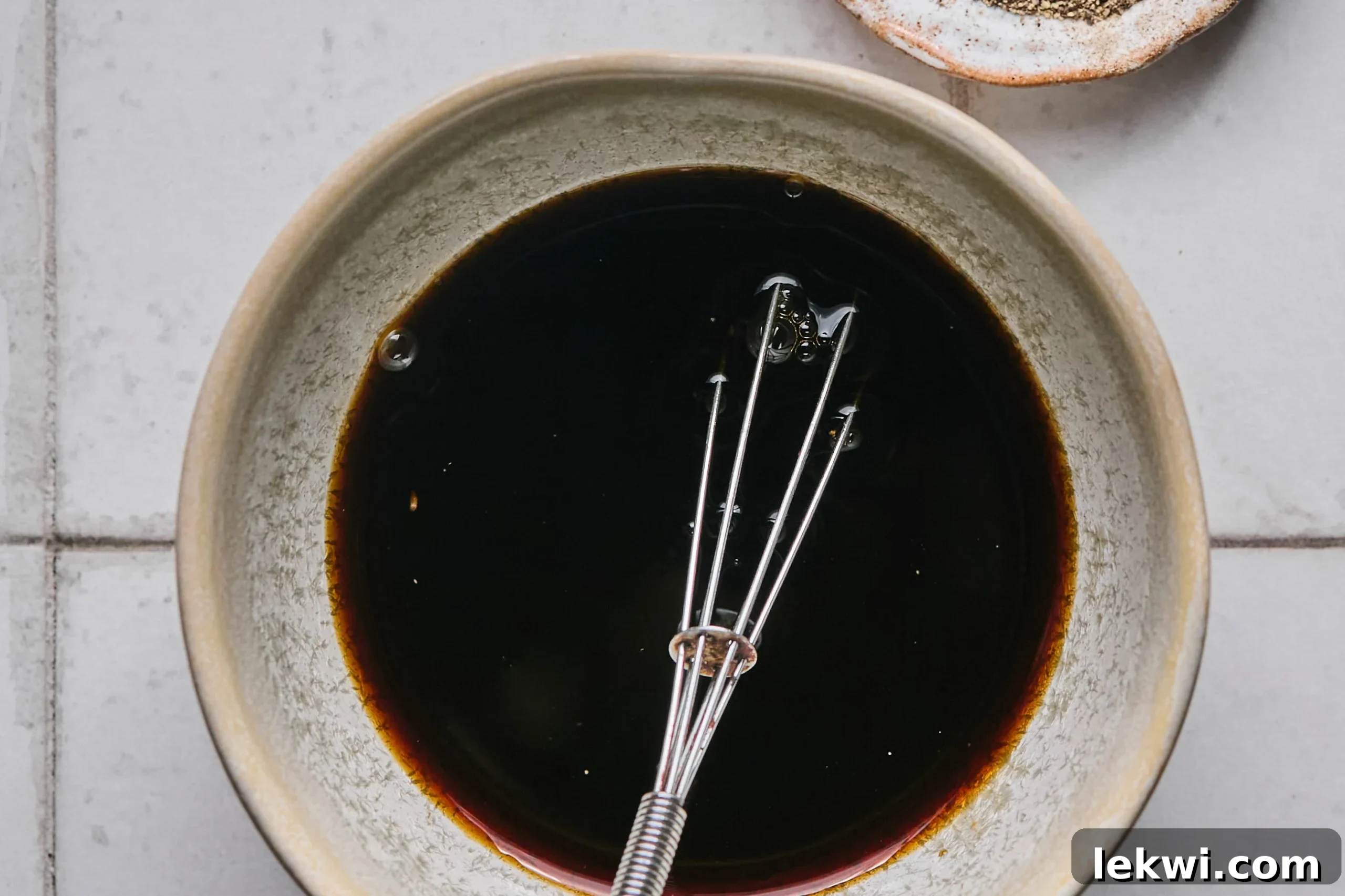 A small bowl holding the mixed Pad Woon Sen sauce, glistening and ready for use, with a whisk resting beside it.