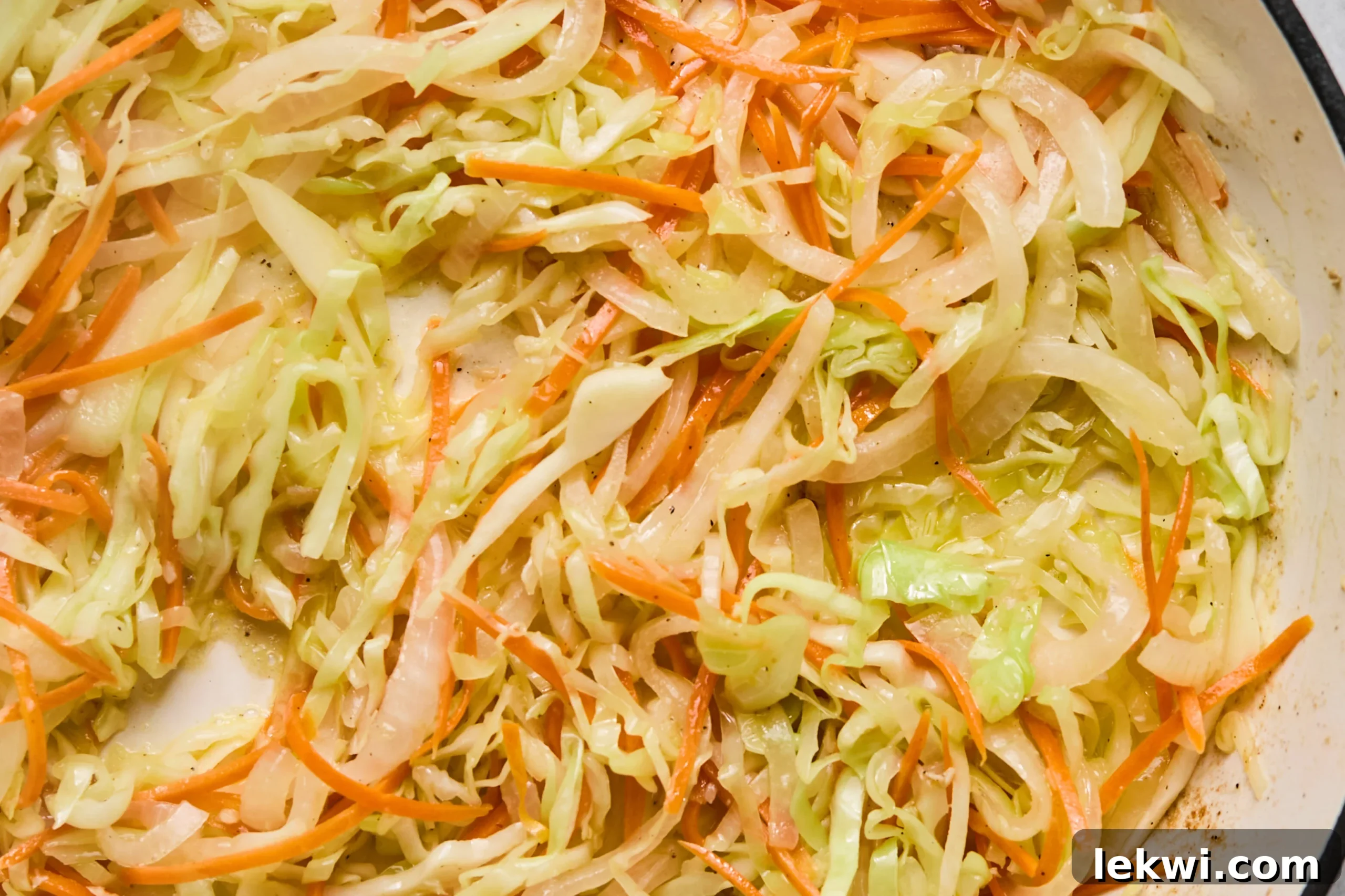 A colorful mix of shredded cabbage, sliced onion, and shredded carrots cooking in a hot pan, becoming tender and fragrant.