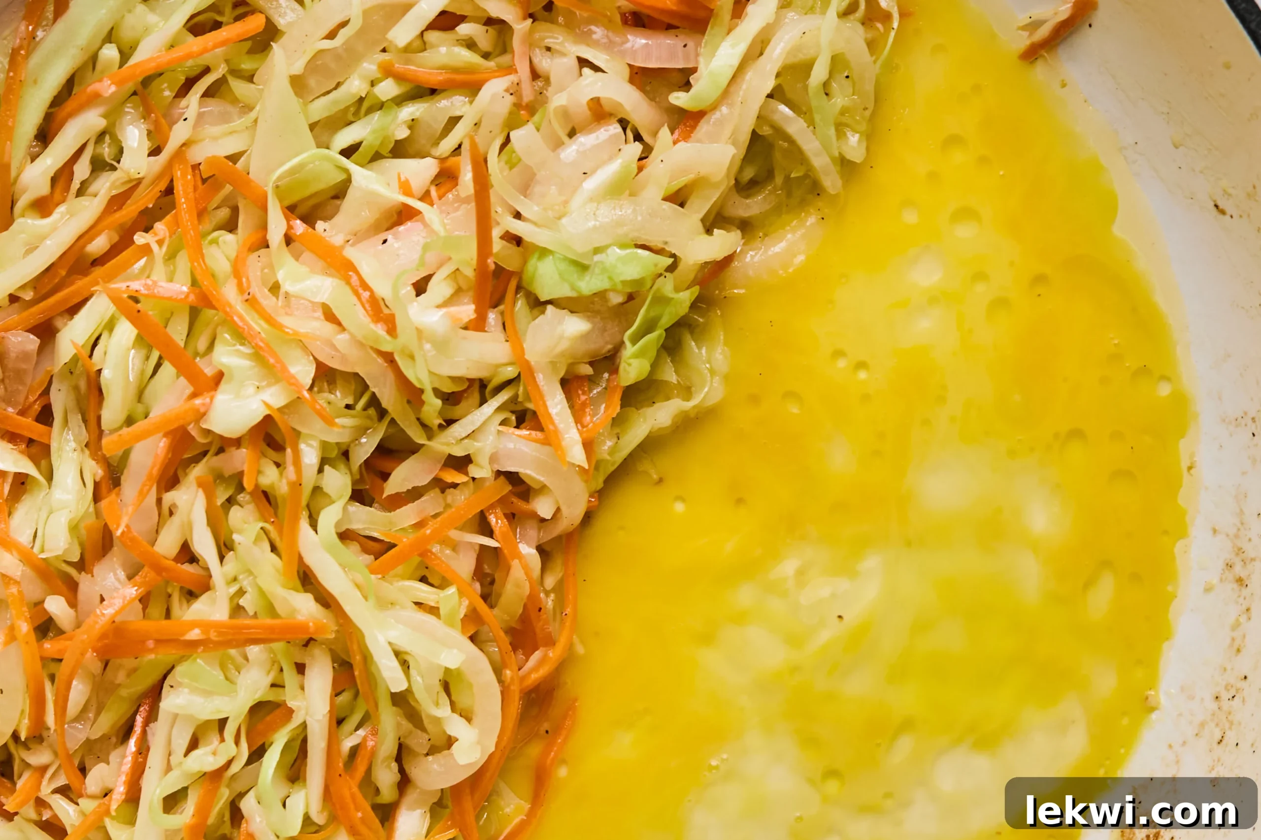 A whisked egg scrambling on one side of a pan, pushed to make space for vegetables already cooked on the other side.