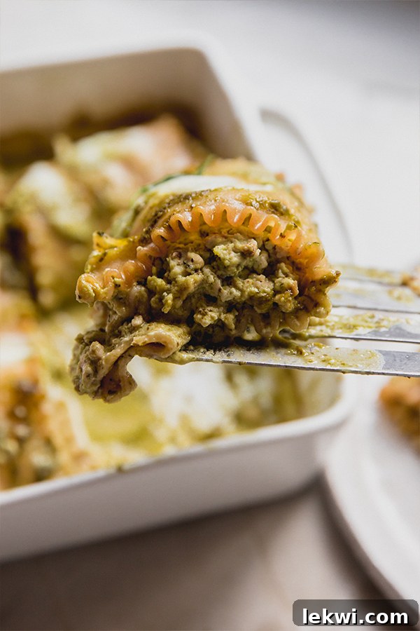 A spatula carefully lifting a single serving of white pesto lasagna roll-ups from a casserole dish, garnished with fresh basil.