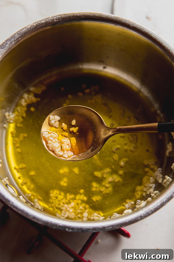 A small, elegant bowl filled with freshly melted ghee infused with fragrant minced garlic, ready to be brushed onto warm breadsticks, promising rich flavor.