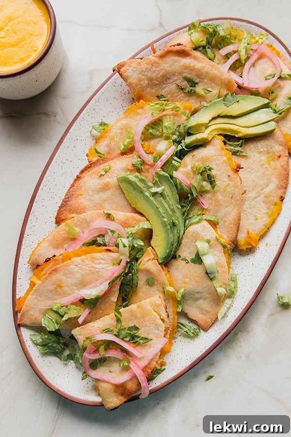 A platter of baked quesadillas topped with avocado and pickled onions.