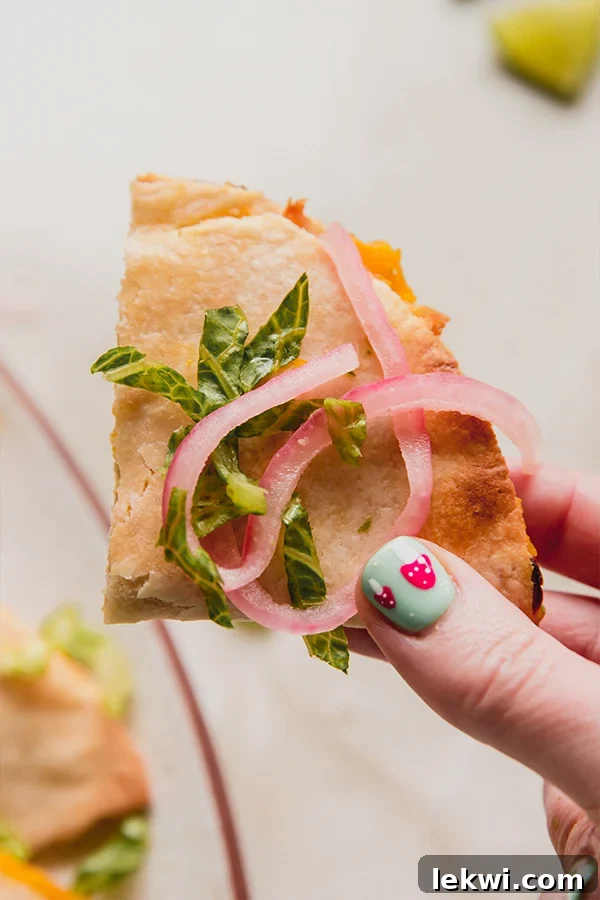 A piece of baked quesadillas with pickled onions in a hand.