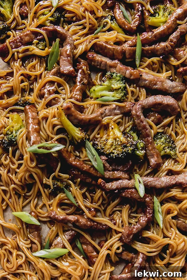 Roasted broccoli and beef, tossed with cooked ramen noodles and coated in a rich, glossy sauce on a sheet pan, ready to be served.
