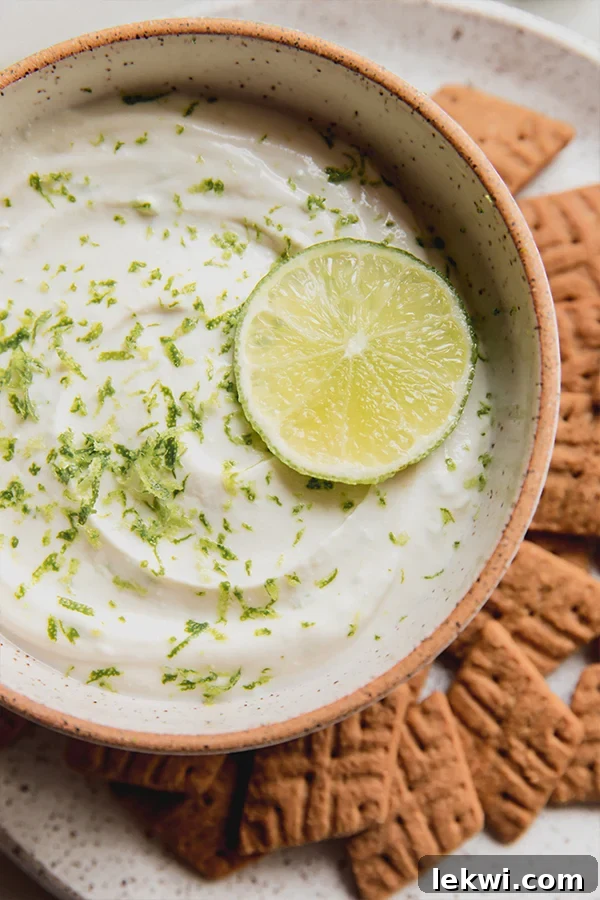 A bowl of vibrant green key lime pie dip, garnished with fresh lime slices and zest, sitting on a rustic wooden surface, perfect for a summer gathering.
