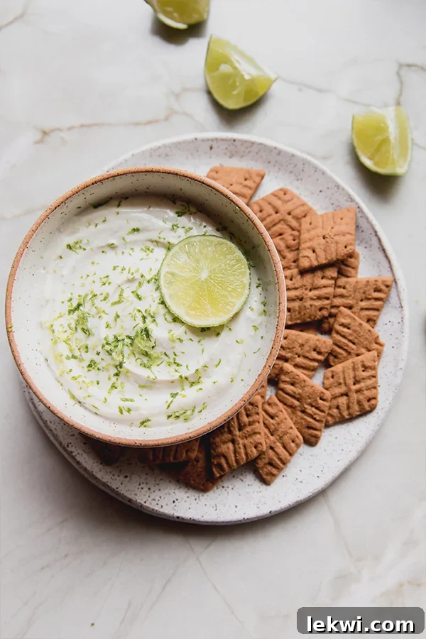 A beautifully presented bowl of creamy key lime pie dip, generously surrounded by an assortment of golden gluten-free graham cracker pieces, ready for dipping and enjoying.