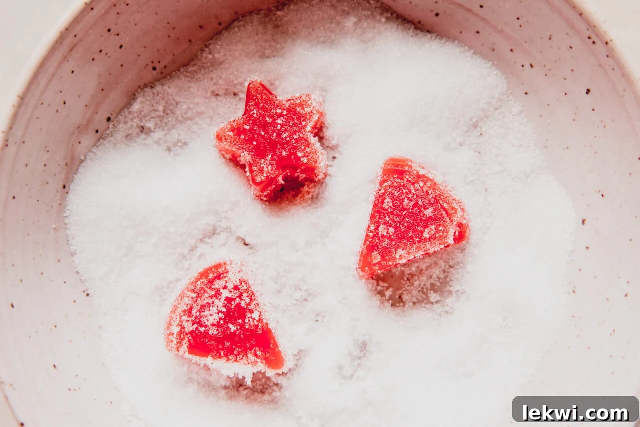 Freshly set sour watermelon gummies being tossed with a granulated sweetener in a bowl to create a tangy coating.