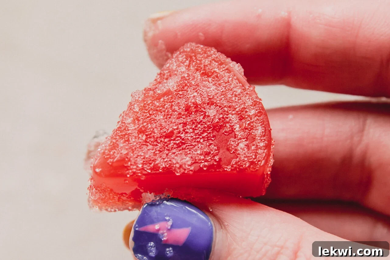 A hand holding a perfectly shaped sour watermelon gummy, showcasing its vibrant color and inviting texture.