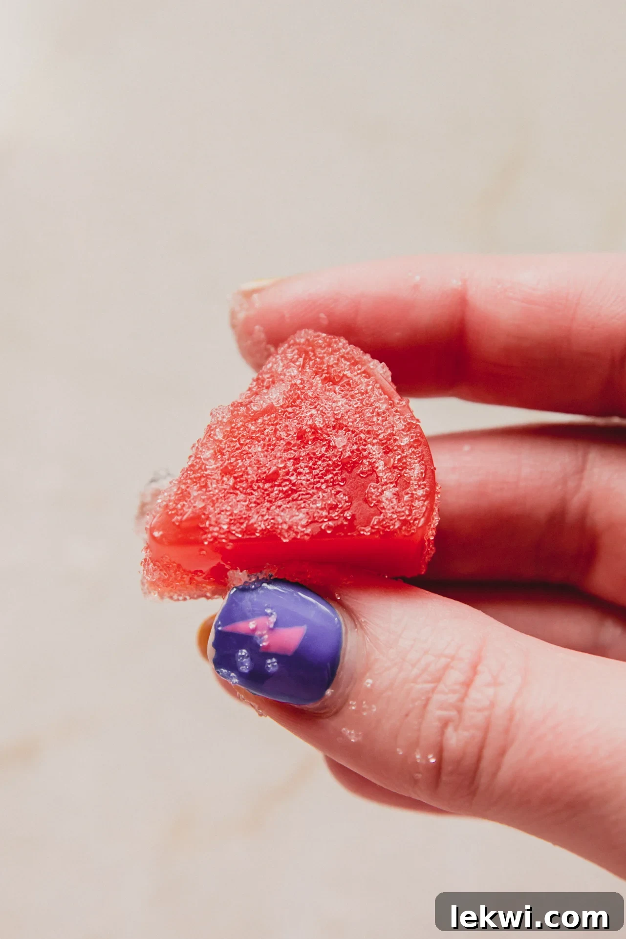 A hand holding a perfectly shaped sour watermelon gummy, showcasing its vibrant color and inviting texture, ready to be enjoyed.