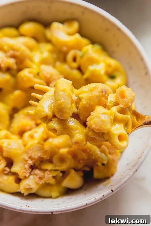 A bowl of zucchini mac and cheese with a fork taking a bite out of it.