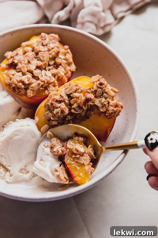 A beautifully plated bowl of air fryer peach crisp, topped with a scoop of dairy-free ice cream, with a spoon taking the first bite.