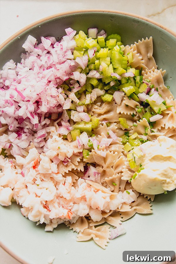 All the freshly prepared ingredients for gluten-free lobster roll pasta salad, including diced lobster, pasta, and vegetables, gathered in a bowl before mixing.