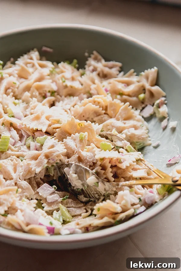 A beautifully presented bowl of gluten-free lobster roll pasta salad, with a serving spoon nestled within, inviting you to take a taste.