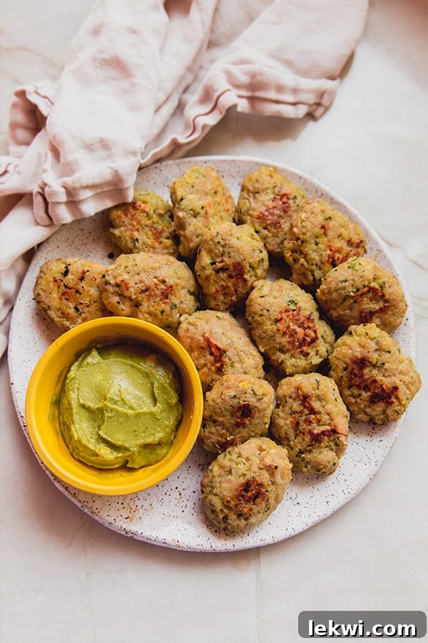 A tantalizing close-up shot of crispy zucchini chicken nuggets arranged artfully on a plate, accompanied by a small bowl of creamy dipping sauce. The golden-brown exterior suggests a satisfying crunch, while the visible texture promises a delightful blend of chicken and vegetables. This image highlights the dish's appeal and its perfect pairing with a favorite dip.