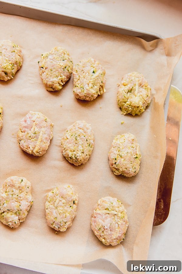 A baking sheet filled with perfectly shaped raw zucchini chicken nuggets, evenly spaced and ready to be cooked. The uniform size of the nuggets suggests careful preparation, promising consistent results. This visual step shows the dish's readiness for the oven.