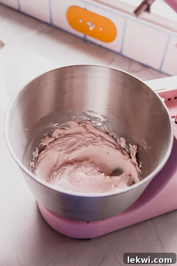 A metal mixing bowl filled with the freshly prepared, fluffy pink icing, ready to be spread.