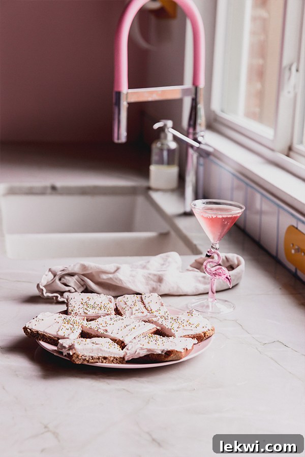 A beautifully arranged plate of funfetti pink sugar cookie bars, frosted and sprinkled, resting on a kitchen counter.
