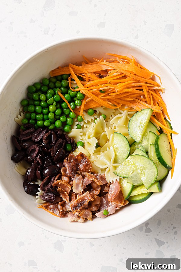 A large mixing bowl containing all the ingredients for bacon ranch bow-tie pasta salad, including pasta, bacon, and vegetables, before being tossed with dressing.