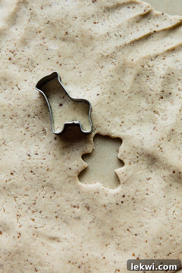 Animal cookie cutters pressing into gluten-free dough on a parchment-lined surface.