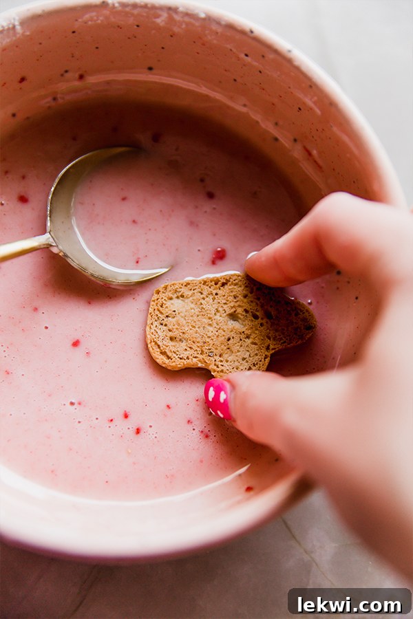 A hand dipping an animal cracker into pink icing.