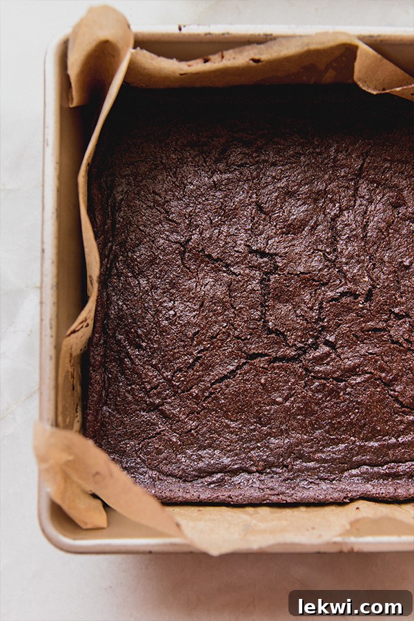 Freshly baked brownies, still warm, in a parchment-lined baking dish, ready for cooling.