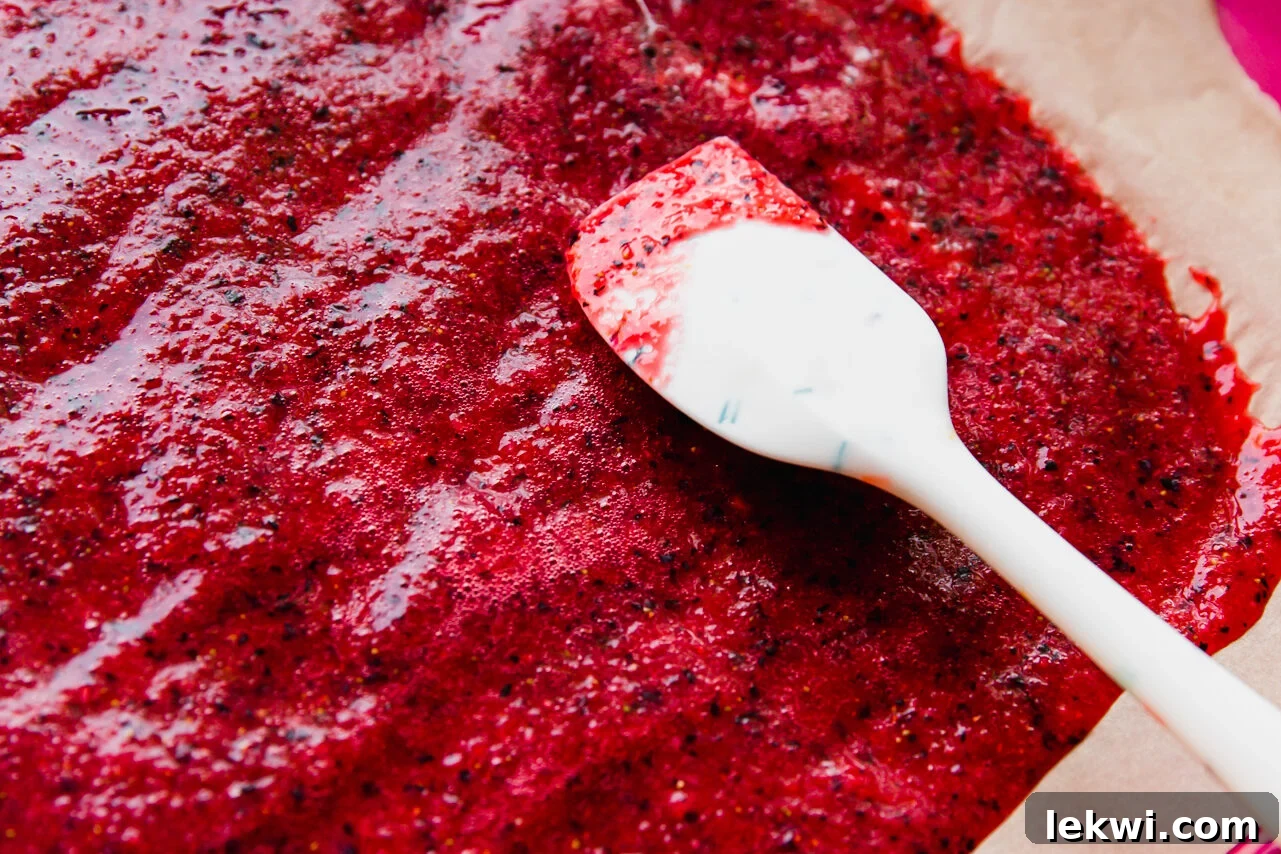 Smooth fruit puree being spread evenly and thinly on a sheet of parchment paper with a silicone spatula.