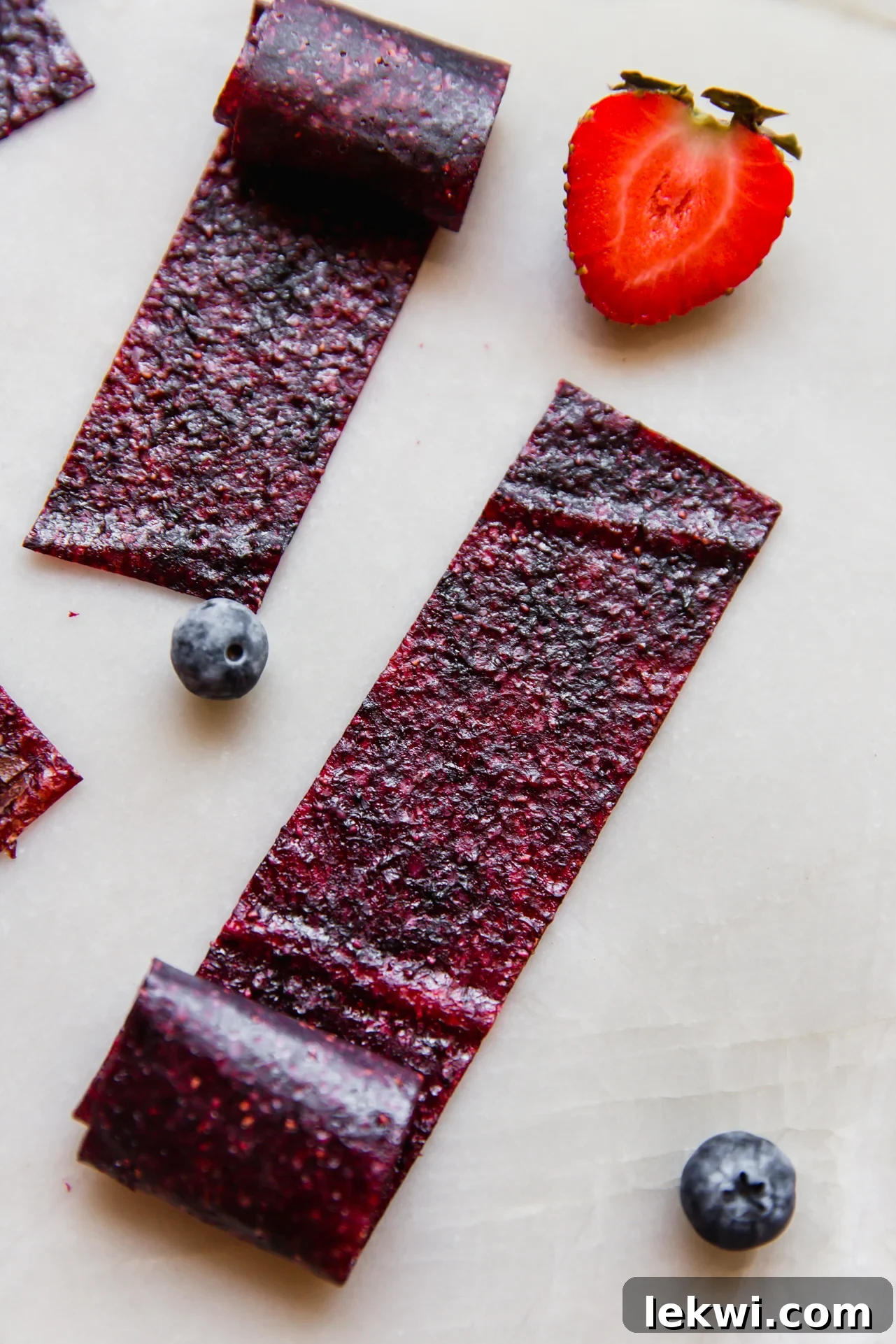 Homemade fruit roll-ups displayed on a white background with fresh strawberries and blueberries, ready to be enjoyed.