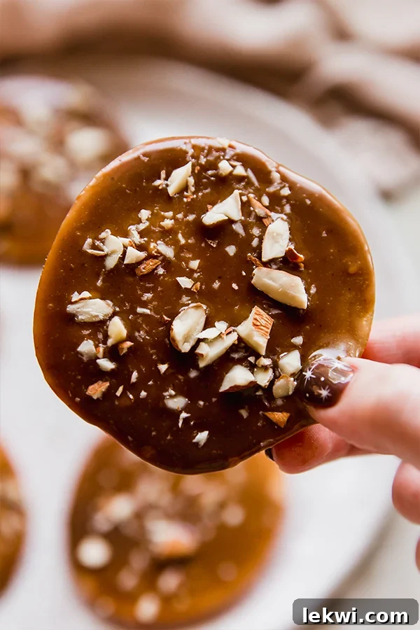 A hand holding a beautifully crafted dairy-free caramel apple slice, topped with crunchy almonds.