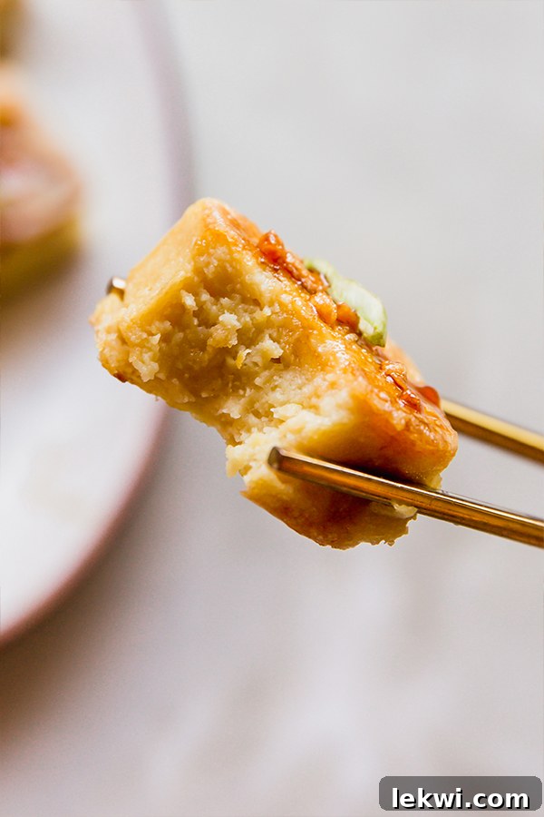 Chopsticks holding a piece of chickpea tofu with a bite taken out, showcasing its texture.