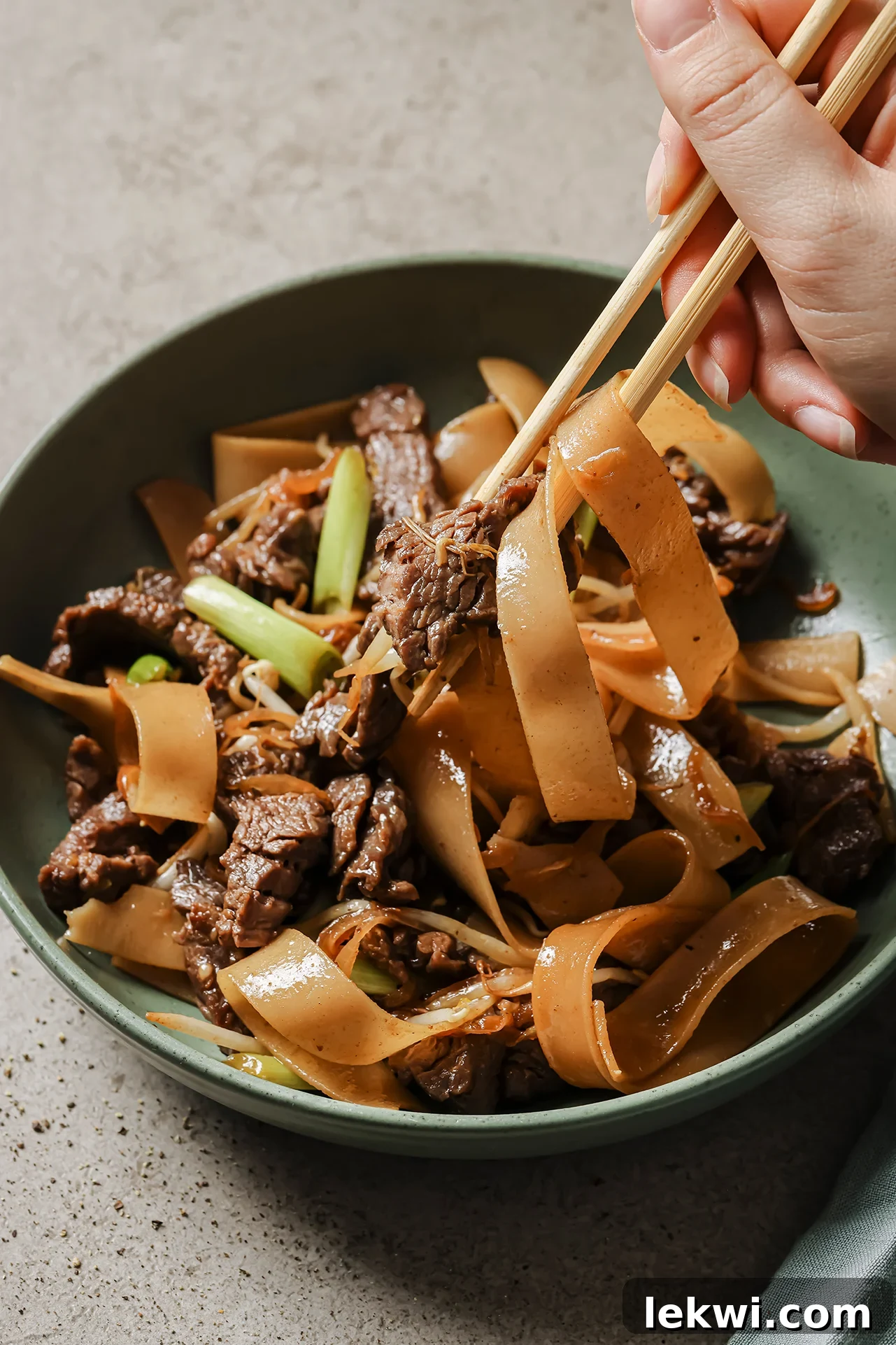 Gluten free beef chow fun in a shallow green bowl with noodles being pulled up with chopsticks. 