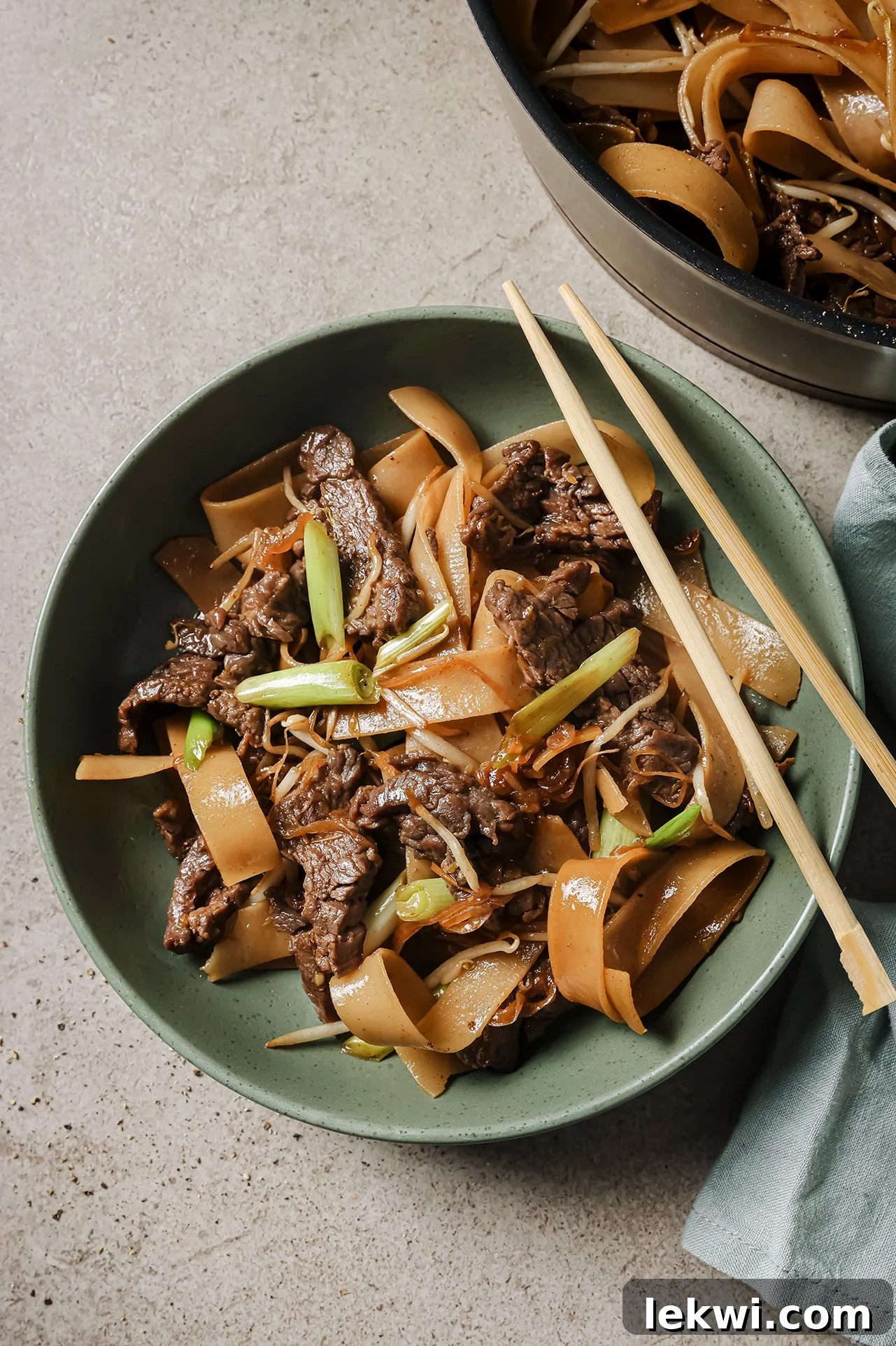Beef chow fun in a large shallow green bowl with chopsticks.